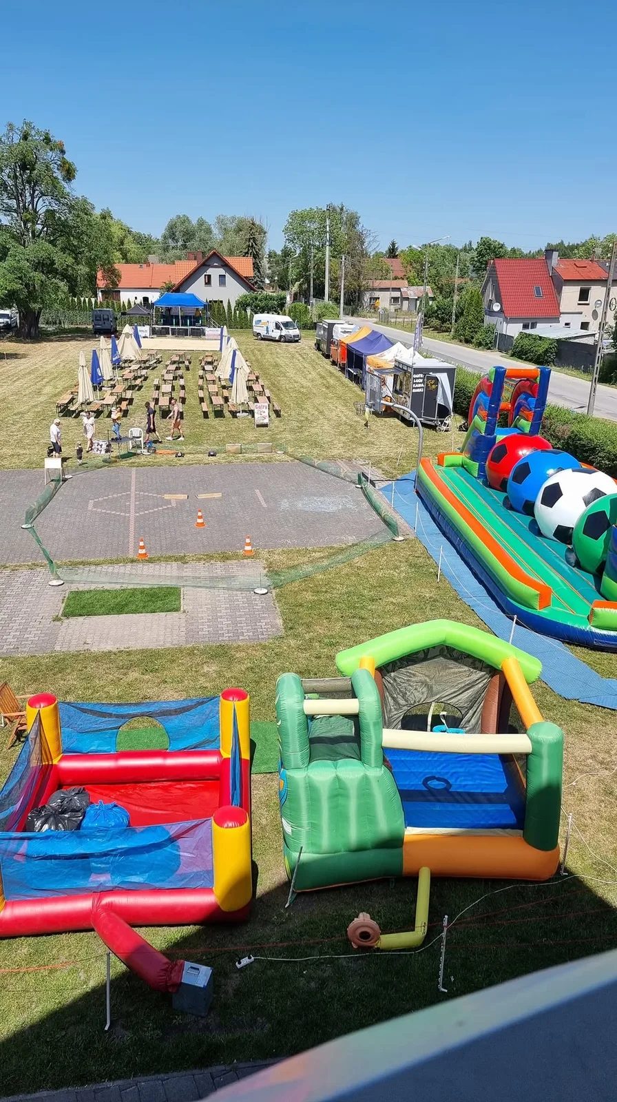 Widok z góry na dmuchańce, stoły i scenę przygotowywane na festyn w czerwcu 2022 roku.